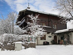 A wooden building with a sloped roof, a staircase leading to an upper level, and a sign indicating a restaurant. - Apartment 4 - Apartment Pension Bäckenhäusl (Uttendorf)