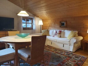 A cozy room with a dining table, wicker chairs, a white sofa, a patterned rug, and wooden walls. - Apartment 4 - Apartment Pension Bäckenhäusl (Uttendorf)
