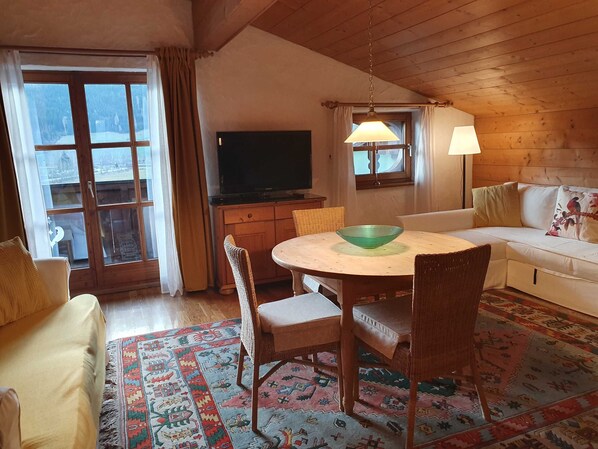 A cozy living room with a round table, wicker chairs, a sofa, a television, and a patterned rug. - Apartment 4 - Apartment Pension Bäckenhäusl (Uttendorf)