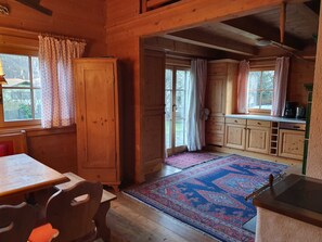 A wooden cabin interior with a dining area, kitchen, and large windows.