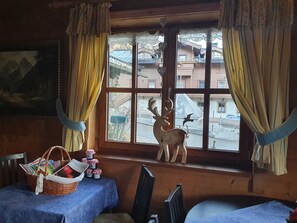 Una habitación con un ventanal grande, una pared de madera, un cuadro, una cesta con objetos y una mesa con mantel azul.