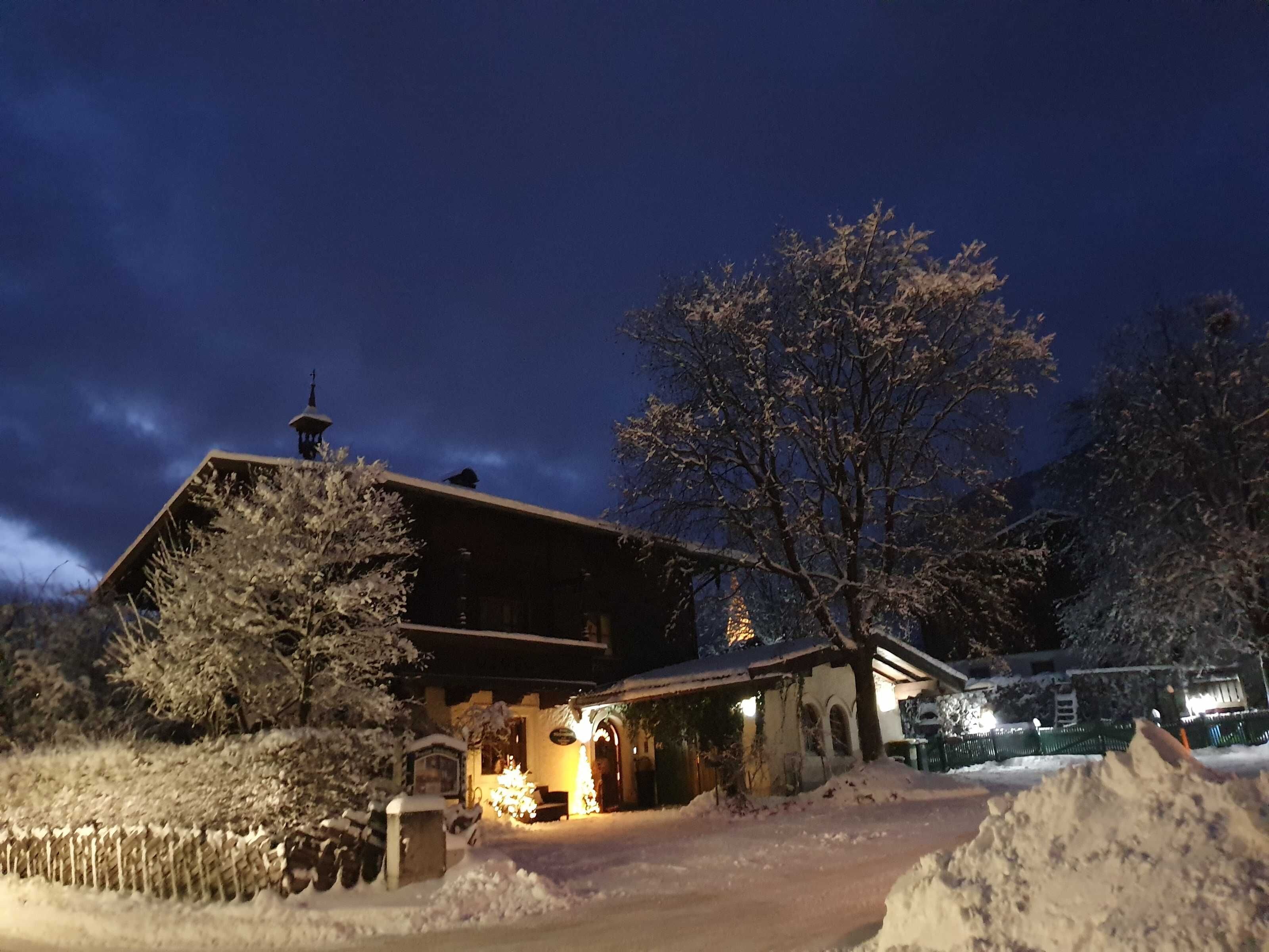 Un bâtiment recouvert de neige, avec un toit en pente, une cheminée bien visible et une allée enneigée.
