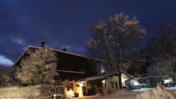 Un bâtiment recouvert de neige, avec un toit en pente, une cheminée bien visible et une allée enneigée.