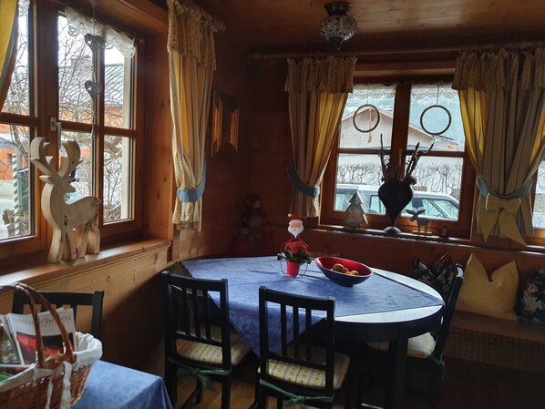 A cozy dining area with a round table, chairs, and a basket of books. - Apartment 4 - Apartment Pension Bäckenhäusl (Uttendorf)