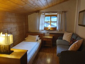 A cozy room with a wooden ceiling, a bed with white bedding, a small table with a lamp, a sofa with cushions, and a window with curtains. - Apartment 4 - Apartment Pension Bäckenhäusl (Uttendorf)