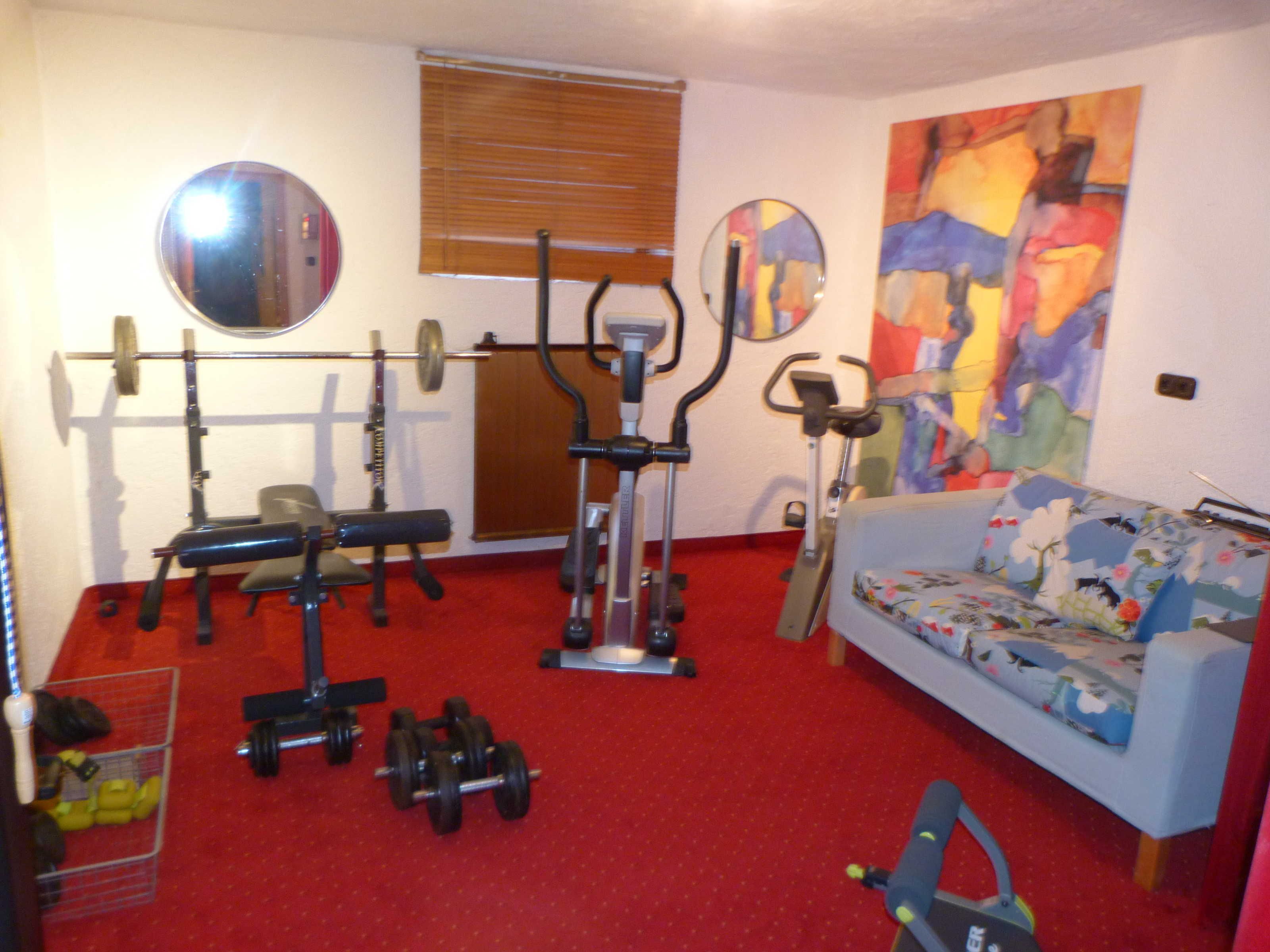 Ein Heimfitnessraum mit Trainingsgeräten, einer Couch und einem großen abstrakten Gemälde.