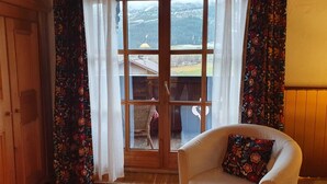 Quarto com uma janela grande, porta de madeira, poltrona branca e tapete estampado.