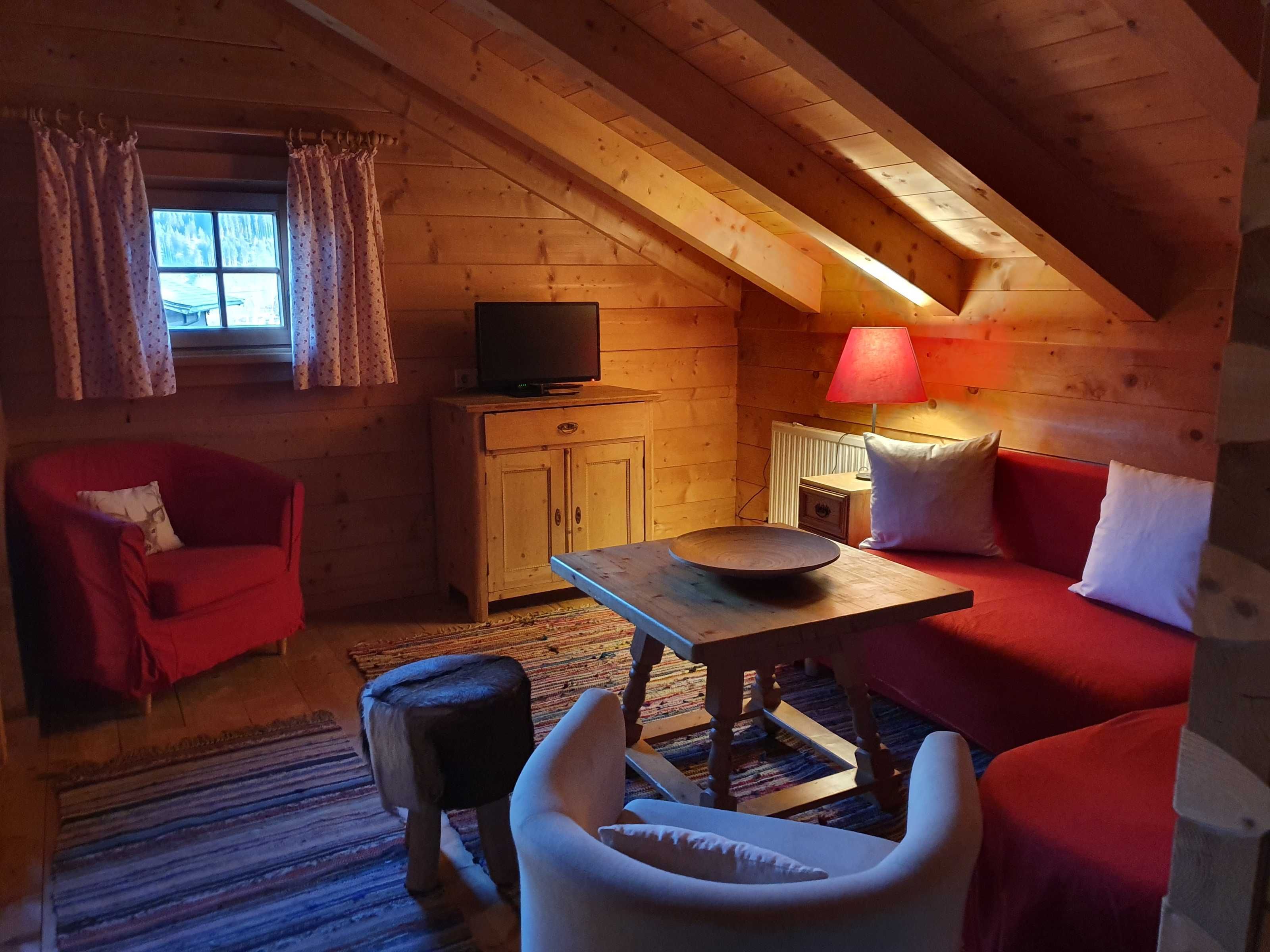 Ein gemütliches Blockhauszimmer mit einem roten Sofa, einem Holztisch, einem Fernseher und einer Lampe.