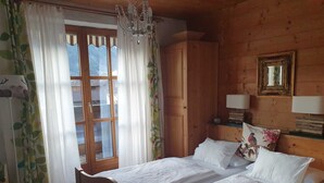 Um quarto de madeira com uma cama, um candelabro, uma janela com cortinas e um espelho na parede.