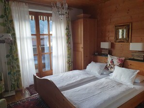 A wooden room with a bed, a chandelier, a window with curtains, and a mirror on the wall.
