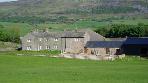A stone farmhouse with a large barn, surrounded by green fields and hills.