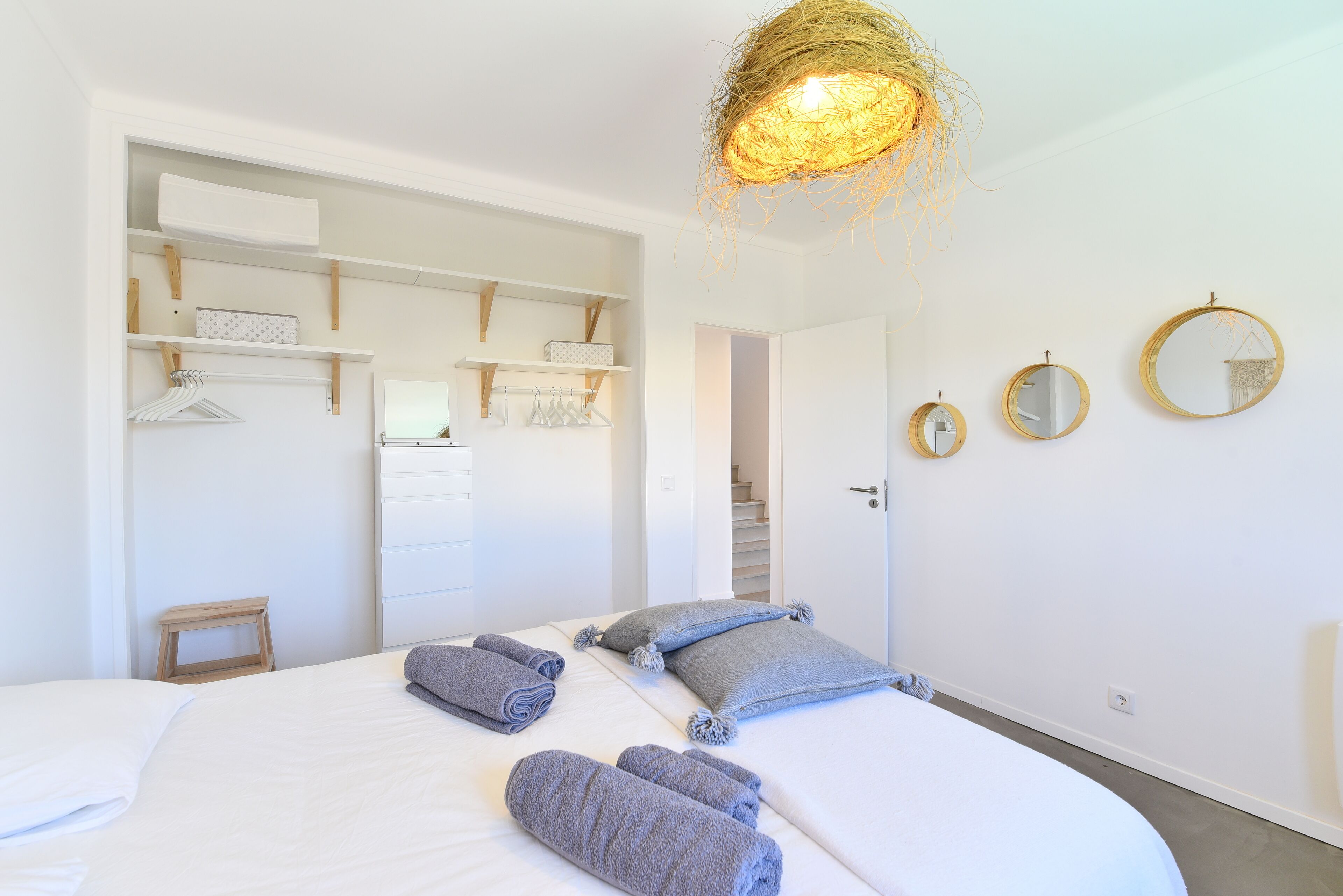 Un dormitorio con una cama grande, dos mesitas de noche, una lámpara colgante y un armario con estantes.