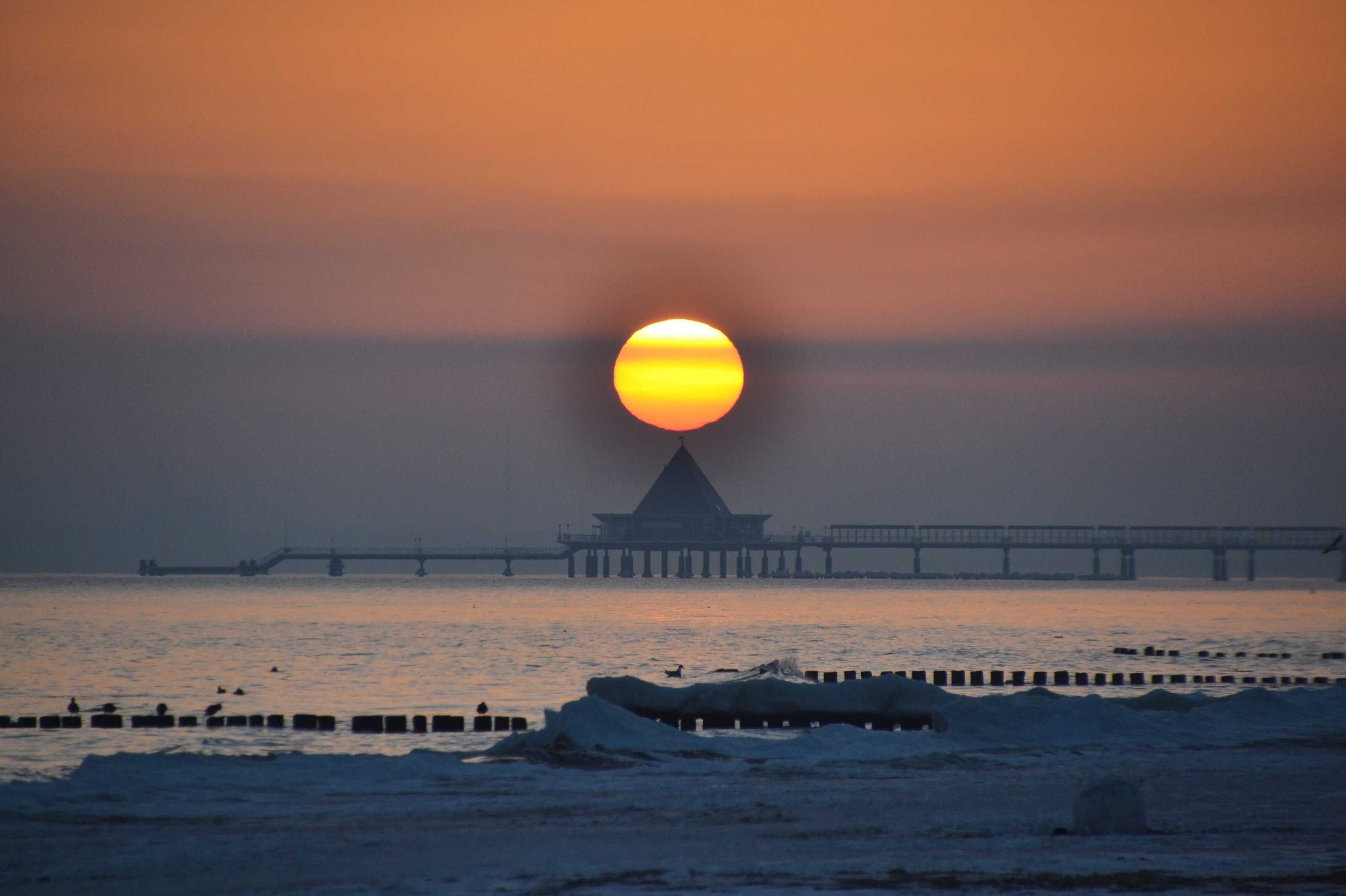 A sunset over a body of water with a pier and a building in the background.