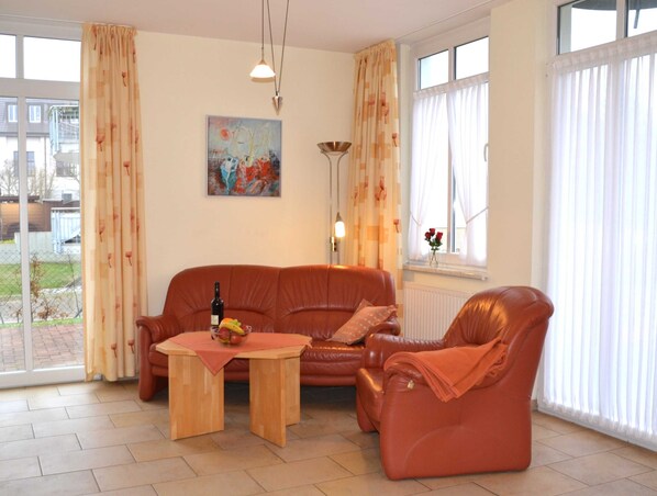 A living room with a sofa, armchair, and a table with a bottle and fruit.