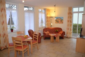 A furnished living room with a dining table, chairs, a sofa, and a small table with a vase.
