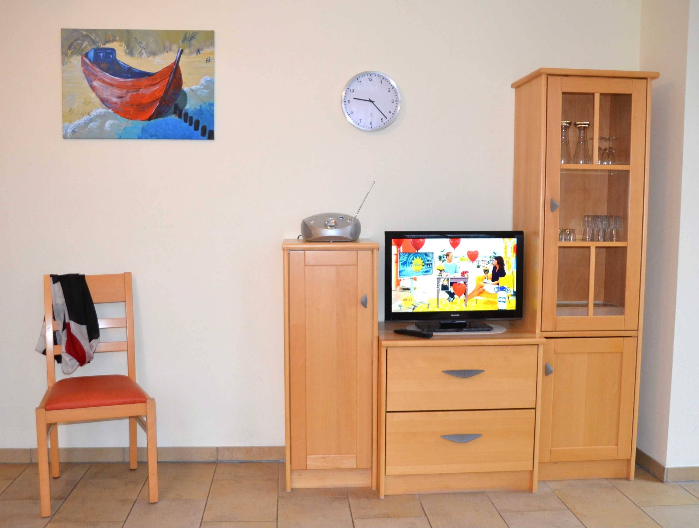 A room with a wooden desk, a television, a clock, a cabinet, and a chair.