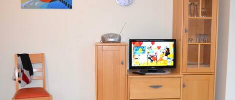 A room with a wooden desk, a television, a clock, a cabinet, and a chair.