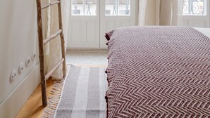 Ein Schlafzimmer mit einem Bett, einer Holzlade, einem Fenster mit Vorhängen und Blick auf Gebäude.