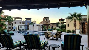 Een buitenzwembadgedeelte met ligbedden en tafels, omgeven door gebouwen in mediterrane stijl.