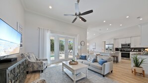 A spacious living room with a large TV, a ceiling fan, and a view to the outside. - Beautiful New Marco Island Home Minutes to Beaches, Parks & Restaurants (Marco Island)