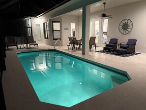 A swimming pool with a clear blue water, surrounded by lounge chairs and a dining area.