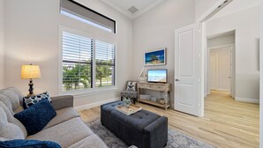 A living room with a sofa, ottoman, and a TV on a wooden stand. - Beautiful New Marco Island Home Minutes to Beaches, Parks & Restaurants (Marco Island)