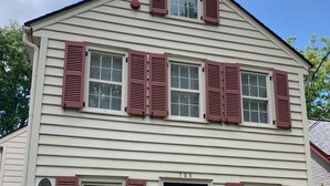 Une maison à deux étages avec une porte d’entrée, de nombreuses fenêtres équipées de volets et des fondations en briques.