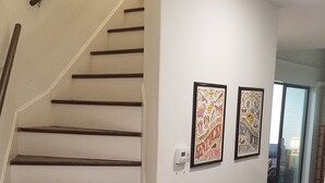 Un escalier avec des marches en bois et une rampe, menant à une pièce dont un mur est blanc et où est accroché un tableau encadré.