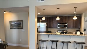 A modern kitchen with dark wood cabinets, stainless steel appliances, and a granite countertop. There are four bar stools under the island. - Two bed two bath plus loft condo in Grand Haven (Grand Haven)