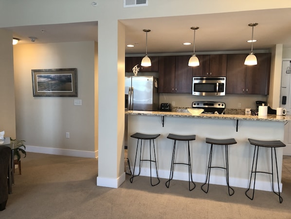 A modern kitchen with dark wood cabinets, stainless steel appliances, and a granite countertop. There are four bar stools under the island.