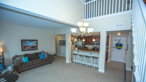 A spacious living room with a sofa, a dining area, and a kitchen with bar stools. - Two bed two bath plus loft condo in Grand Haven (Grand Haven)