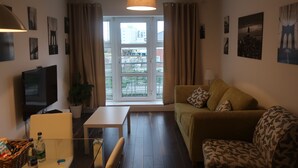 A living room with a sofa, a television, a table, and a window with curtains. - Grand Canal Dock Corporate Apartment (Dublin)