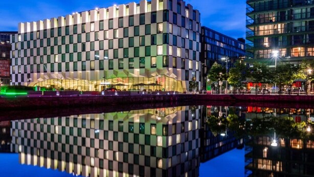 A modern building with a checkered facade reflecting on a calm water body. - Grand Canal Dock Corporate Apartment (Dublin)