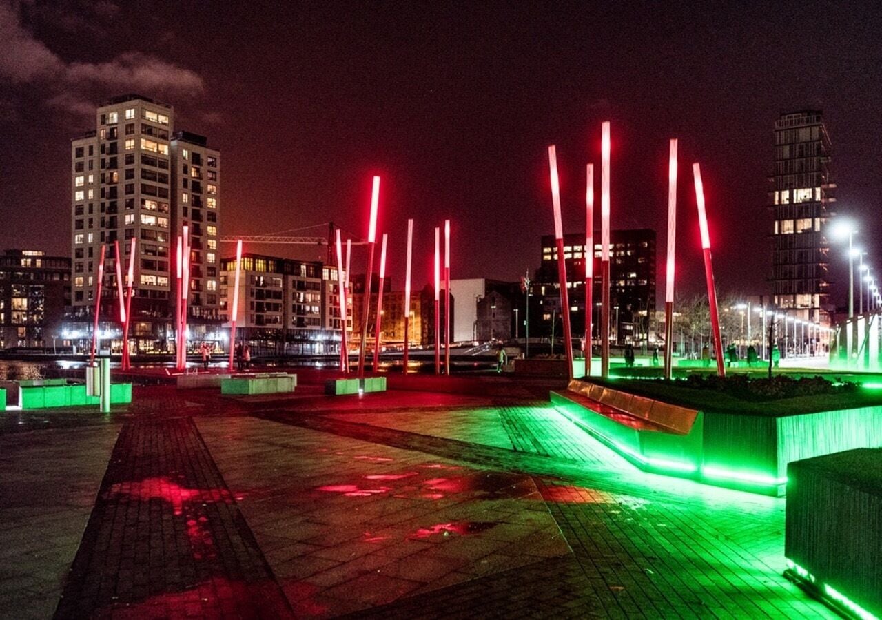 Een verlicht stadsbeeld 's nachts met gebouwen en een promenade aan het water.