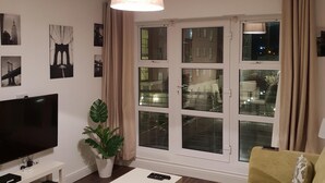 A living room with a flat-screen TV, a white coffee table, a sofa, a potted plant, and a large window with curtains. - Grand Canal Dock Corporate Apartment (Dublin)