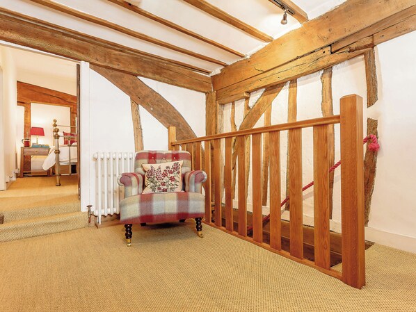 A room with a high ceiling, exposed wooden beams, a plaid armchair with a floral pillow, and a wooden gate.