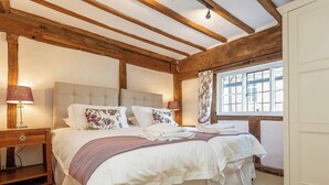Een slaapkamer met een groot bed, houten balken, een nachtkastje en een raam met gordijnen.