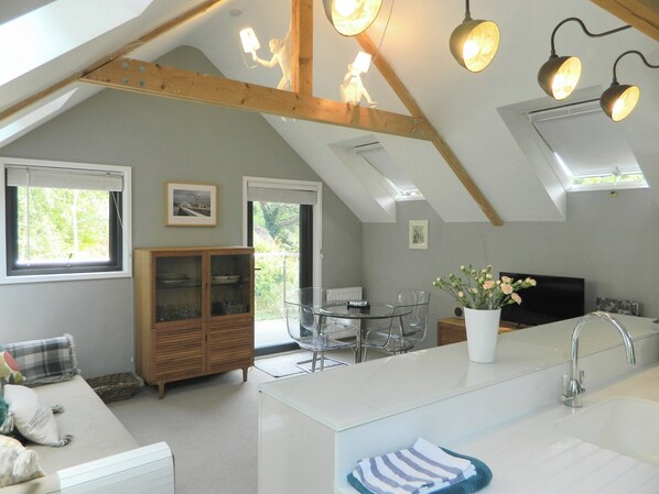 A modern kitchen with a central island, a dining area with a glass table, and a view of the outdoors through a window.