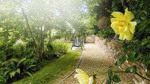 Un camí de jardí amb una paret de maó a un costat i vegetació exuberant a l'altre.