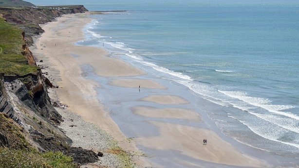 Una platja costanera amb un penya-segat rocos, sorra i mar tranquil·la.