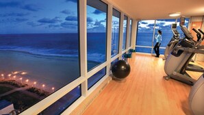A gym with large windows overlooking a beach at dusk.
