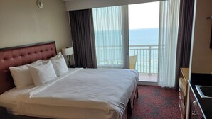 A hotel room with a large bed, a nightstand, a lamp, a view of the ocean, and a balcony.