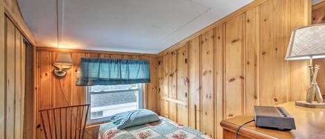 Een kamer met houten lambrisering, een bed met quilt, een stoel, een bureau met lamp en een raam met blinds.