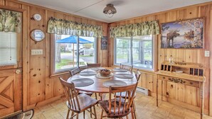 L’intérieur d’un chalet en bois comprend une table de salle à manger ronde, des chaises, une petite table d’appoint en bois et un tableau représentant un élan.