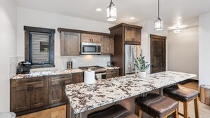 A modern kitchen with dark wood cabinets, a large marble countertop, stainless steel appliances, and pendant lighting. - Modern Condo in Downtown Whitefish, Prime Location (Whitefish)
