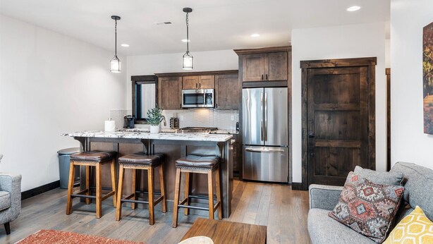 A modern kitchen with stainless steel appliances, a marble countertop, and wooden stools. - Modern Condo in Downtown Whitefish, Prime Location (Whitefish)