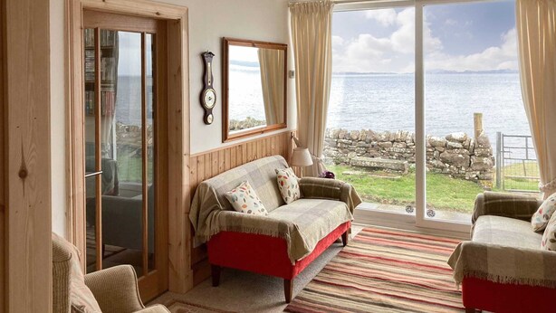 A cozy room with a red sofa, a wooden chair, and a view of the sea through large windows.
