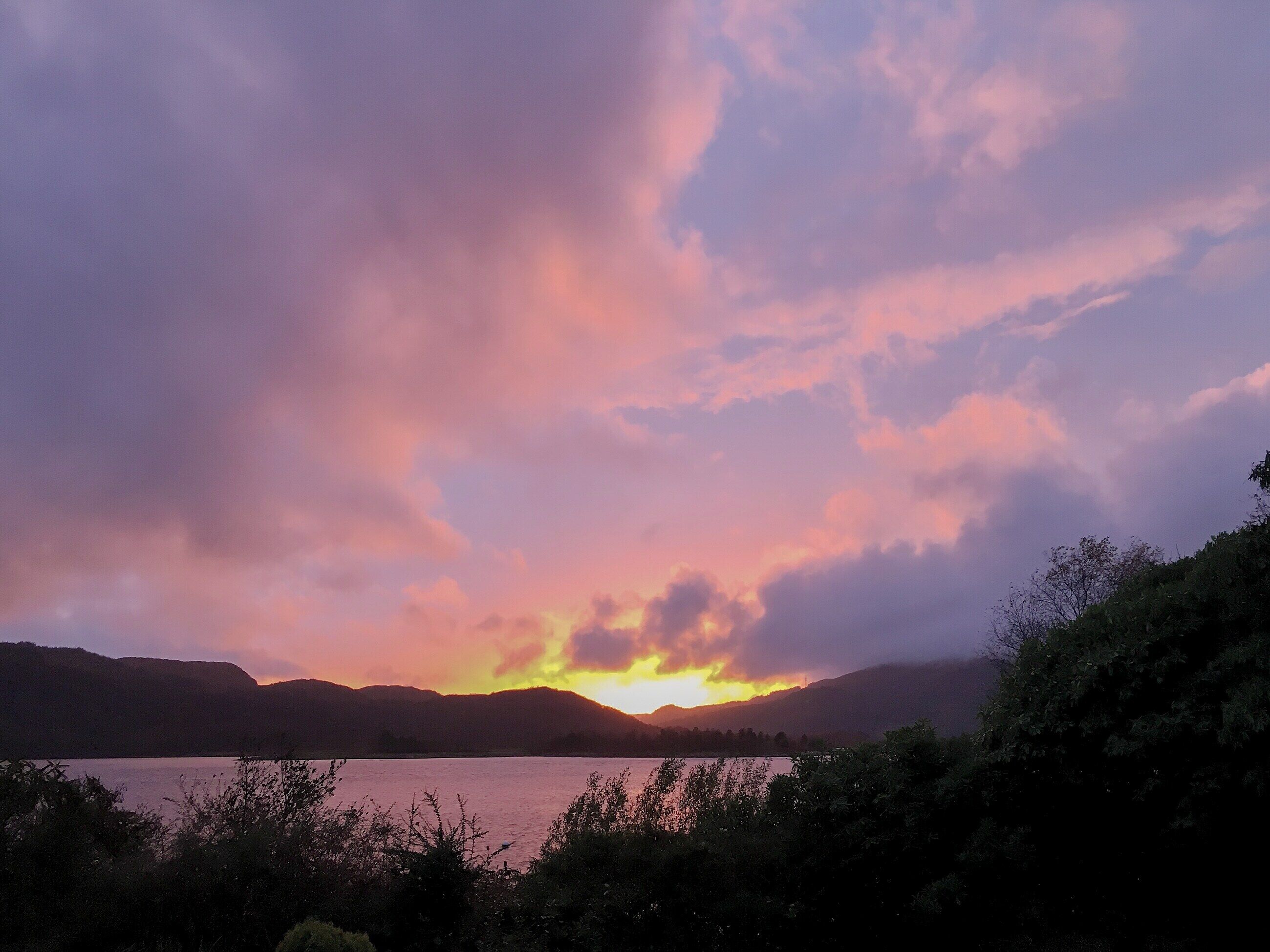 Un coucher de soleil sur un lac, avec des montagnes en arrière-plan.