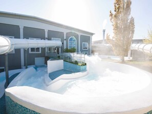 Un área de spa con un jacuzzi, una piscina y un edificio de amplios ventanales y chimenea.