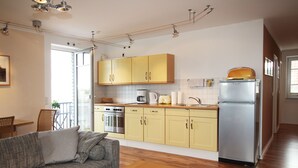 Una cucina compatta con mobili gialli, un frigorifero in acciaio inossidabile e un'area pranzo con divano e tavolo.